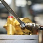 A Beta Tools 1/2-inch combination wrench tightening a bolt on a brass hydraulic assembly, highlighting precision and control in tight spaces. Get it at Wrenchers.com.
