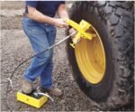 Operator using an ESCO hydraulic bead breaker on a large off-road tire while activating the foot-operated hydraulic pump on the ground
