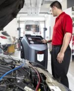 Automotive technician operating the Robinair 34998 A/C service machine during a vehicle HVAC procedure, highlighting its advanced controls and user-friendly operation