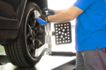 Technician installing an AC200-style wheel alignment clamp on a vehicle tire while standing on a lift
