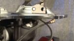 Close-up of a tire changer’s built-in bead sealing jets, showing the metal mounting plate, valve connection, and flexible air hose routed beneath the assembly