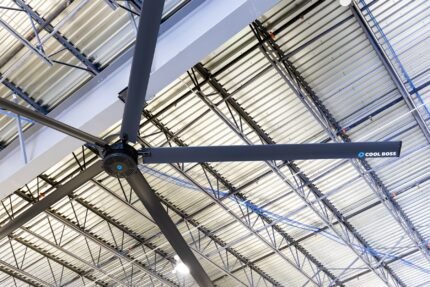 Close-up of the Cool Boss CB-24 HVLS fan installed in a steel beam warehouse ceiling, highlighting the Cool Boss logo and industrial mounting hardware