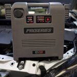 DSR ProSeries DSR119 portable jump starter in use on a vehicle, positioned on an engine bay with its charging and battery status lights visible. Get it at Wrenchers.com
