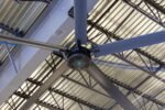 Cool Boss CB-11 HVLS industrial ceiling fan mounted to a warehouse beam, showing five aluminum blades and a black center motor hub with blue Cool Boss logo
