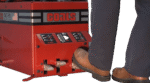 Operator pressing the foot pedals on a Coats RC-55 tire changer, showing the red control panel, labeled clamp and rotation controls, and the machine’s base