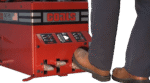 Operator pressing the foot pedals on a Coats RC-45A tire changer, showing the red control panel with clamp and rotation controls and the machine’s lower chassis