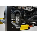 Side view of an SUV on a four-post alignment lift highlighting yellow wheel stops and low-profile runway design
