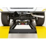 Rear differential and suspension visible on a truck raised on a four-post alignment lift with center jack positioned between runways