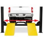 Rear view of a pickup truck positioned on a four-post alignment lift with yellow approach ramps and arrows indicating adjustable runway width