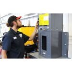 Technician operating a Ranger RP-50HD industrial oil filter crusher in a workshop environment, using the upper control panel